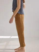 Pantalón largo de lino color marrón, con corte cigarette, tiro alto, bolsillos laterales y traseros con pespuntes a la vista, y etiqueta de cuero con logo en la cintura.