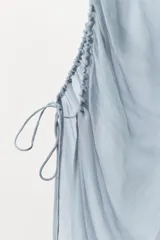 Top celeste semitransparente de escote pico y tirantes finos. Detalle de drapeado lateral ajustable con cordones.