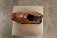 Zueco negro con textura croco, diseño tipo mocasín y tira regulable al talón.