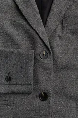 Blazer gris jaspeado de corte entallado, con solapas de muesca, cierre de dos botones, bolsillo superior insertado y bolsillos delanteros con solapa. Tiene hombreras, botonadura frontal, botón decorativo en los puños y abertura atrás.