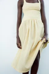Vestido midi color amarillo pálido con textura arrugada, escote cuadrado, tirantes anchos y falda acampanada.