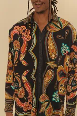 Camisa de poliéster negra con estampado de cachemir en tonos naranja, marrón, celeste y amarillo. Tiene cuello clásico, mangas largas y cierre frontal con botones.