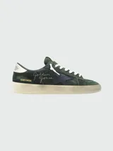 Zapatillas Golden Goose modelo Stardan, confeccionadas en gamuza verde oscuro con detalles en cuero liso azul marino en la estrella lateral. Presentan cordones blancos y una suela de goma desgastada color crema. El lateral lleva la inscripción manuscrita "Golden Goose" y la referencia "GGDB/STARDAN".