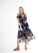 Vestido midi de algodón italiano, color azul marino con estampado en tonos blanco, beige y naranja/marrón. Presenta mangas cortas tipo murciélago, cuello en V con botones frontales y lazo desmontable para ajustar a la cintura.