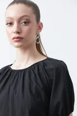 Top negro de manga corta con escote redondo y frunces en la costura de la sisa, creando un efecto de manga abullonada. El tejido parece ligero y con textura.