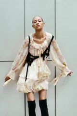 Vestido corto con estampado floral en tonos pastel, cuello redondo con volantes y escote pico ajustable con lazadas. Manga larga acabada en puño con lazadas y bajo con pliegues.