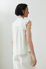 Camisa sin mangas color verde agua con cuello mao, cierre frontal con botones y detalle de puntilla en los hombros.