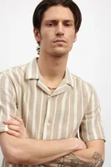 Camisa de manga corta con cuello resort y cierre frontal con botones. Diseño a rayas verticales en tonos beige y blanco.