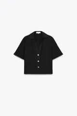 Camisa negra de manga corta con cuello solapa y escote pico. Detalle de nido de abeja en la espalda y cierre frontal con botones.