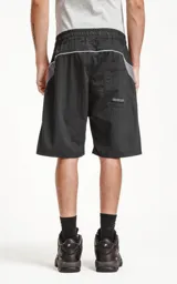 Bermuda negra con recortes blancos y grises, calce oversize, textil liviano, elástico en la cintura, cordón de ajuste, bolsillos delanteros y traseros.