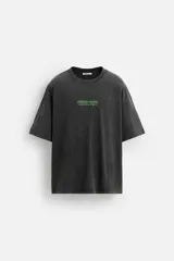 Camiseta gris oscuro con efecto lavado, cuello redondo, manga corta y estampado de textos combinados en verde neón en el delantero y la espalda.