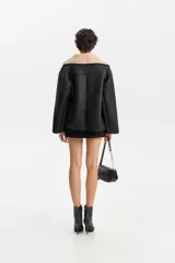 Chaqueta corta de poliéster con efecto cuero en color negro e interior de corderito beige. Presenta un diseño de corte holgado con solapas anchas, cierre cruzado y bolsillos laterales.