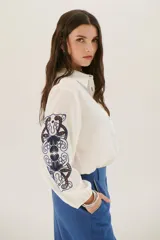 Camisa blanca de manga larga con bordados florales marrones en las mangas.