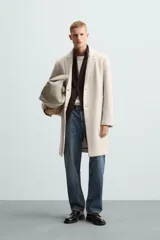 Abrigo straight fit color beige confeccionado en tejido con lana. Cuello con solapas de muesca, manga larga acabada en puño con botones, bolsillos de vivo en cadera, detalle de bolsillo interior y bajo con abertura en centro espalda. Cierre frontal de botonadura.