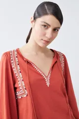 Remera blanca de estilo boho con bordados en el escote y mangas largas. Presenta escote en V con lazos y borlas. Corte recto y holgado.