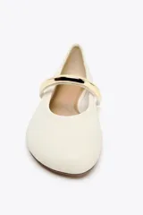 Zapato tipo bailarina color crema con acabado en punta redonda y tira sobre el empeine con aplique metálico dorado.