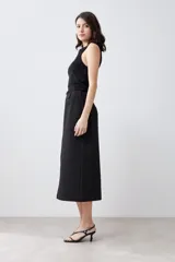 Falda midi negra de corte recto, con tajo lateral y cinturón con hebilla metálica.