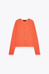 Chaqueta color naranja de punto con cuello redondo y manga larga. Detalle de tejido doble capa combinado en color blanco en el ruedo. Cierre frontal con botones.