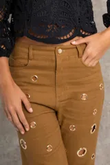 Pantalón de jean color marrón con corte recto, tiro alto y detalle de ojalillos metálicos grandes a lo largo de las piernas.