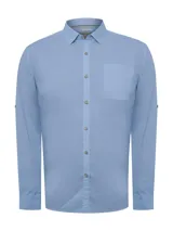 Camisa de manga larga celeste, confeccionada en popelina de algodón orgánico. Cuenta con botones de madera, mangas ajustables, bolsillo de pecho con logo bordado y protección UPF +20.