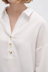 Blusa blanca holgada de poliéster con cuello camisero y mangas largas.