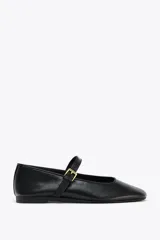 Zapato plano tipo bailarina en piel color negro, con tira sobre el empeine y hebilla metálica ajustable.