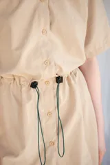 Vestido corto verde militar de microfibra con cuello camisero negro, cintura elastizada con cordón de ajuste y mangas cortas con dobladillo. Cierre frontal con botones.