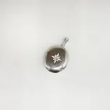 Dije relicario ovalado de plata 925 con circonias incrustadas en el asa y en el centro, formando una flor de ocho pétalos.