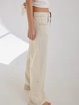 Pantalón gris de tiro medio alto, corte ancho, con bolsillos delanteros y traseros, detalles de atraques y triples costuras en color amarillo.