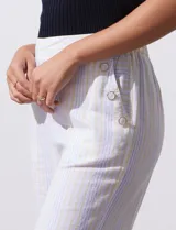 Pantalón capri de lino color blanco con rayas verticales celestes y amarillas, pretina elastizada, bolsillos delanteros y botones decorativos.