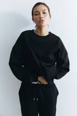 Buzo negro liso, de corte oversized con cuello redondo y hombros caídos. Presenta puños y bajo acanalados.