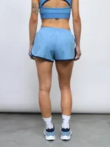 Short deportivo de mujer color azul marino con ribetes blancos en los bordes. Presenta un parche con el escudo del Club Nacional de Football en la pierna izquierda y el logo de Umbro en la derecha.