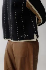 Chaqueta corta de lana color negro con detalles en beige y marrón. Tiene cuello mao, cierre frontal con botones y bolsillos de parche.