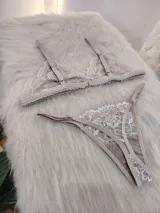 Conjunto de lencería color nude, compuesto por un bralette triangular de encaje floral con tirantes finos y una tanga regulable clásica de encaje a juego.