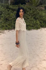 Vestido largo color crudo, tejido a crochet con diseño calado. Tiene cuello redondo, mangas cortas con volados y forro interior.