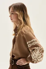 Camisa de calce holgado color marrón camel, confeccionada en Lyocell, con bordados blancos de estilo folclórico en las mangas.