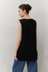 Blusa sin mangas negra de punto suave y fluido, con silueta larga y recta. Presenta botones dorados en los laterales.