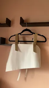 Top corto de ecocuero blanco con breteles anchos de ecocuero negro con textura de cocodrilo y hebillas metálicas.