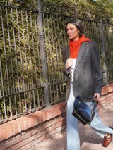 Blazer oversize con diseño asimétrico que combina dos tweeds contrastantes: uno marrón liso y otro blanco y negro con estampado pata de gallo. Tiene botones de strass y un pin de salchicha.
