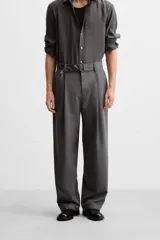 Pantalón negro de corte ancho con cinturón de tela con hebilla metálica y pliegues frontales.