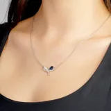 Gargantilla plateada con dije de lazo con una piedra azul en forma de lágrima.