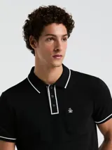 Chomba negra de piqué con cuello clásico, tapeta de dos botones y bolsillo de parche en el pecho con logo bordado. Detalles de ribete blanco en cuello y mangas.