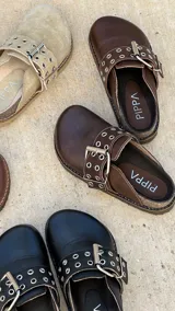 Zueco marrón de cuero con hebilla metálica ajustable, plantilla de cuero y suela de goma.