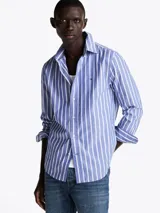 Camisa de popelín de algodón a rayas verticales azules y blancas, de corte regular, con cuello abotonado, puños redondeados con botón y logo de Tommy Hilfiger bordado en el pecho.