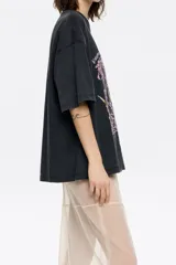 Remera negra de algodón con cuello redondo y manga corta. Estampado frontal con diseño floral abstracto en tonos rosa y marrón.