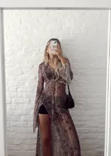 Vestido largo de gasa transparente con estampado de piel de serpiente en tonos marrones. Tiene cuello camisero, mangas largas acampanadas y abertura frontal con cordones.