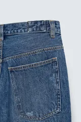 Bermuda de jean azul con lavado medio, corte holgado, cinco bolsillos, roturas y cierre frontal con cremallera y botón.