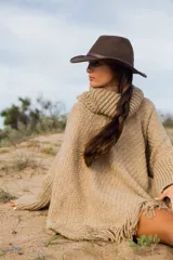 Poncho de tejido grueso color beige, con cuello alto y flecos en el ruedo.