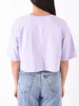 Remera corta lila con estampado de texto 'Spread Your Kindness' con flores amarillas.