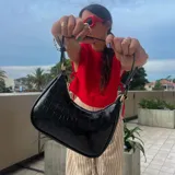 Cartera de hombro negra, estilo baguette, con acabado charol y textura de cocodrilo. Posee correa corta ajustable con detalle de nudo y herrajes dorados.